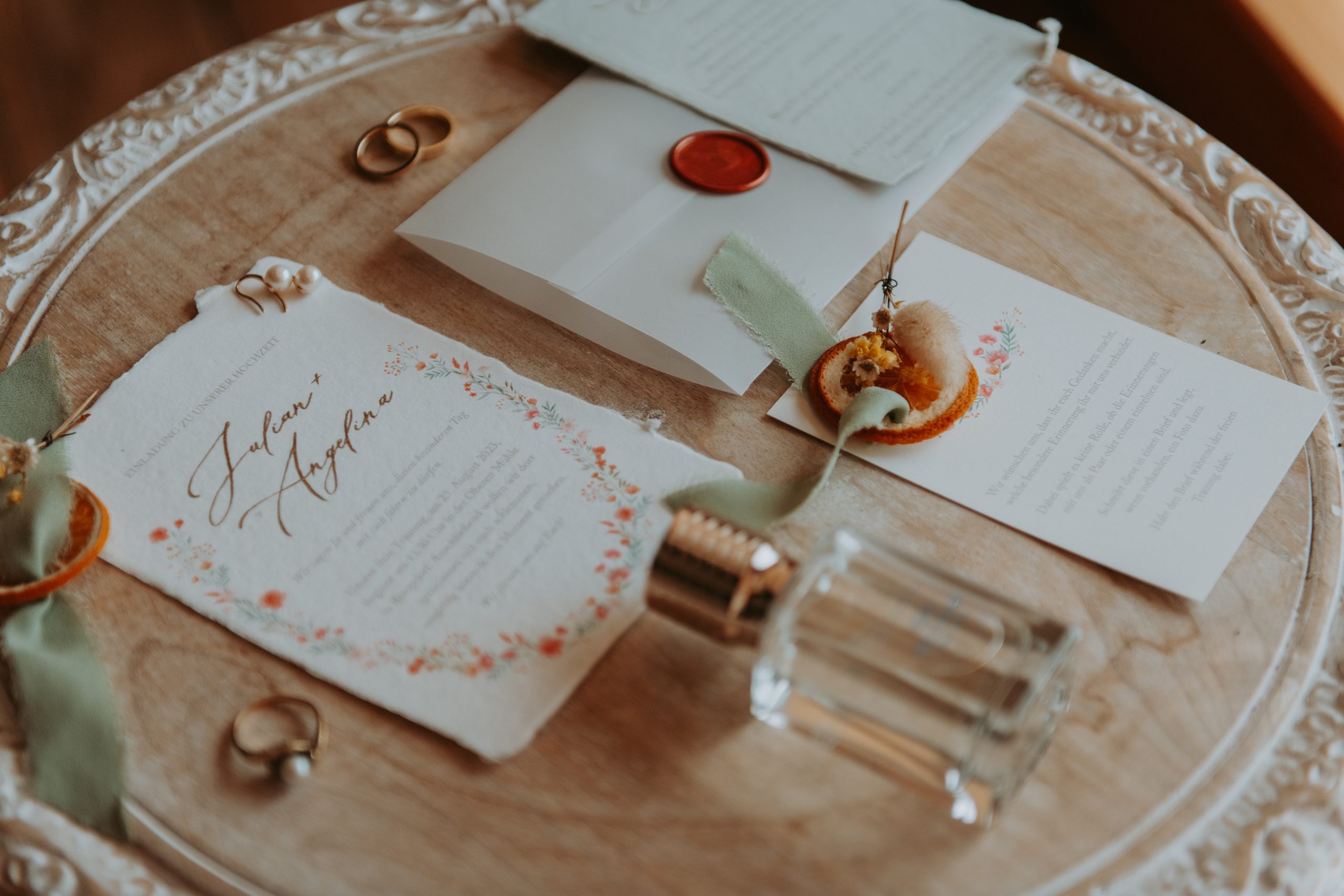 Detailfotos während der Hochzeit bestehend aus Parfüm, Ringen, Einladungen und Dekorationsdetails wie Tüchern und Orangen.